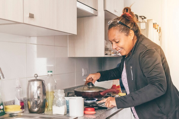 smiling woman tending to covered skillet on stovetop