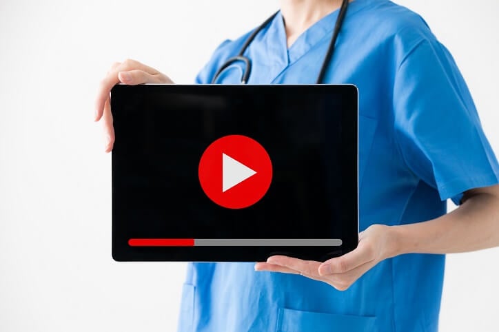woman in scrubs holding black screen with red play arrow woman in scrubs holding black screen with red play arrow