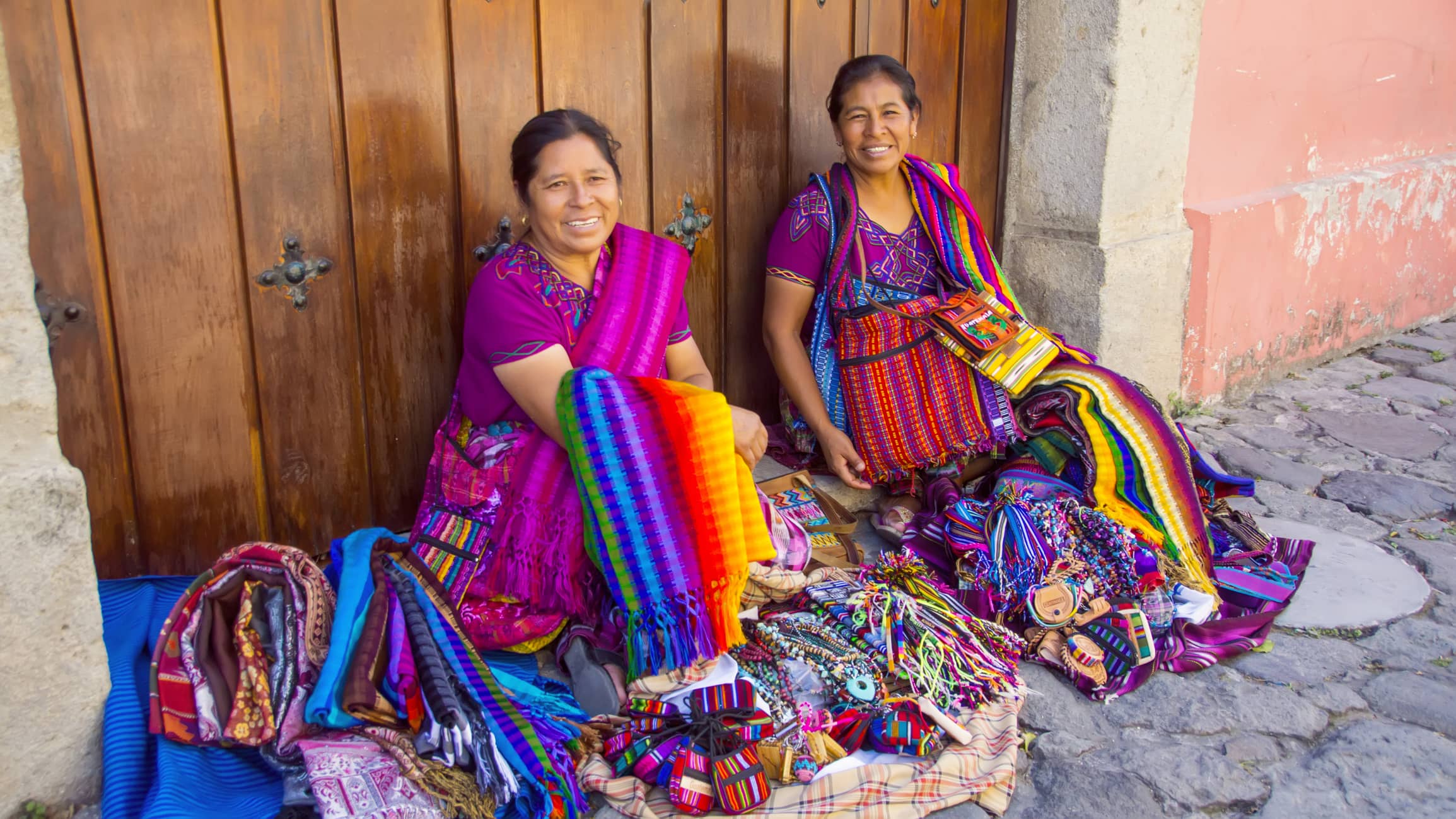 2 Guatemalan native women sit on side of road in colorful customary costumes 2 Guatemalan native women sit on side of road in colorful customary costumes