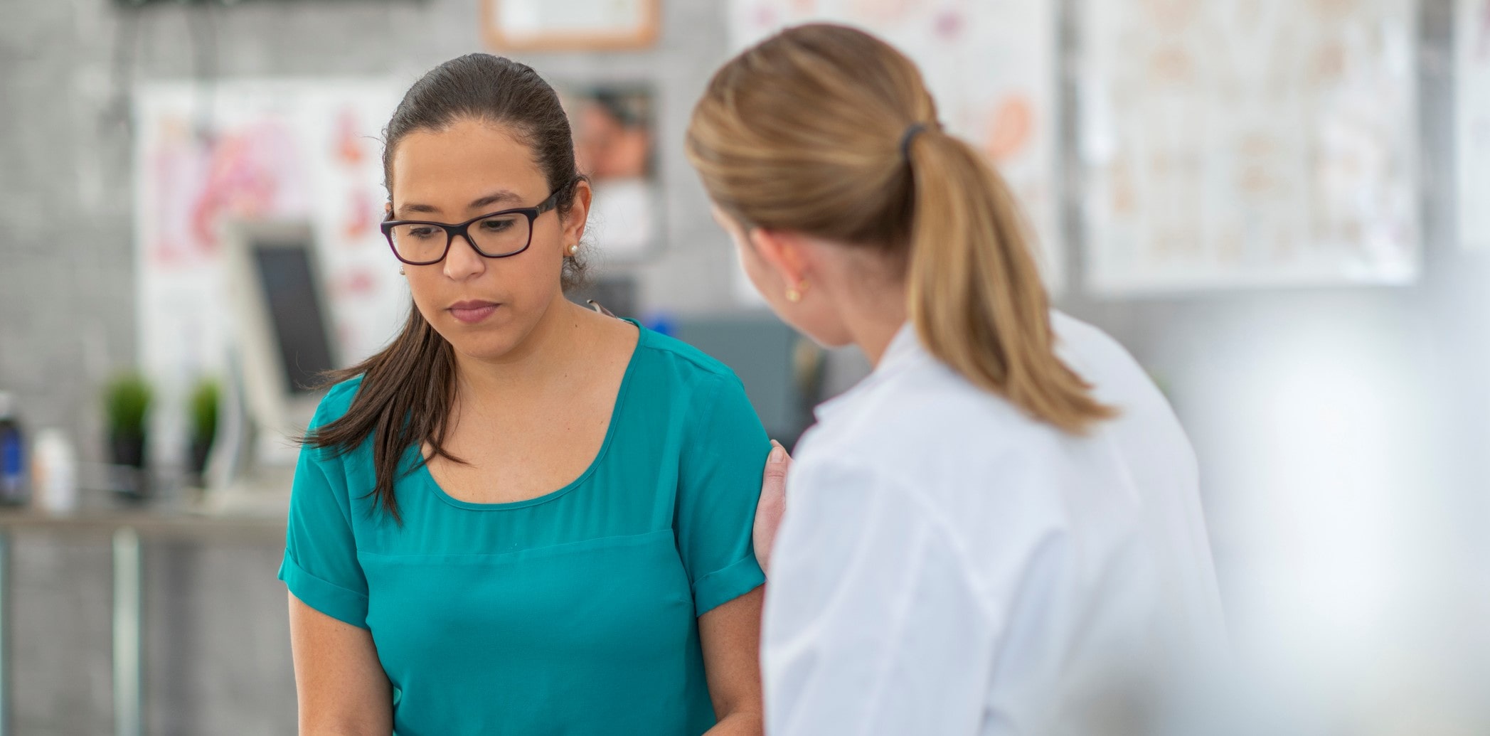 white brunette female in green scrubs and glasses looking down, in trouble, white female nurse sitting next to her, comforting her white brunette female in green scrubs and glasses looking down, in trouble, white female nurse sitting next to her, comforting her