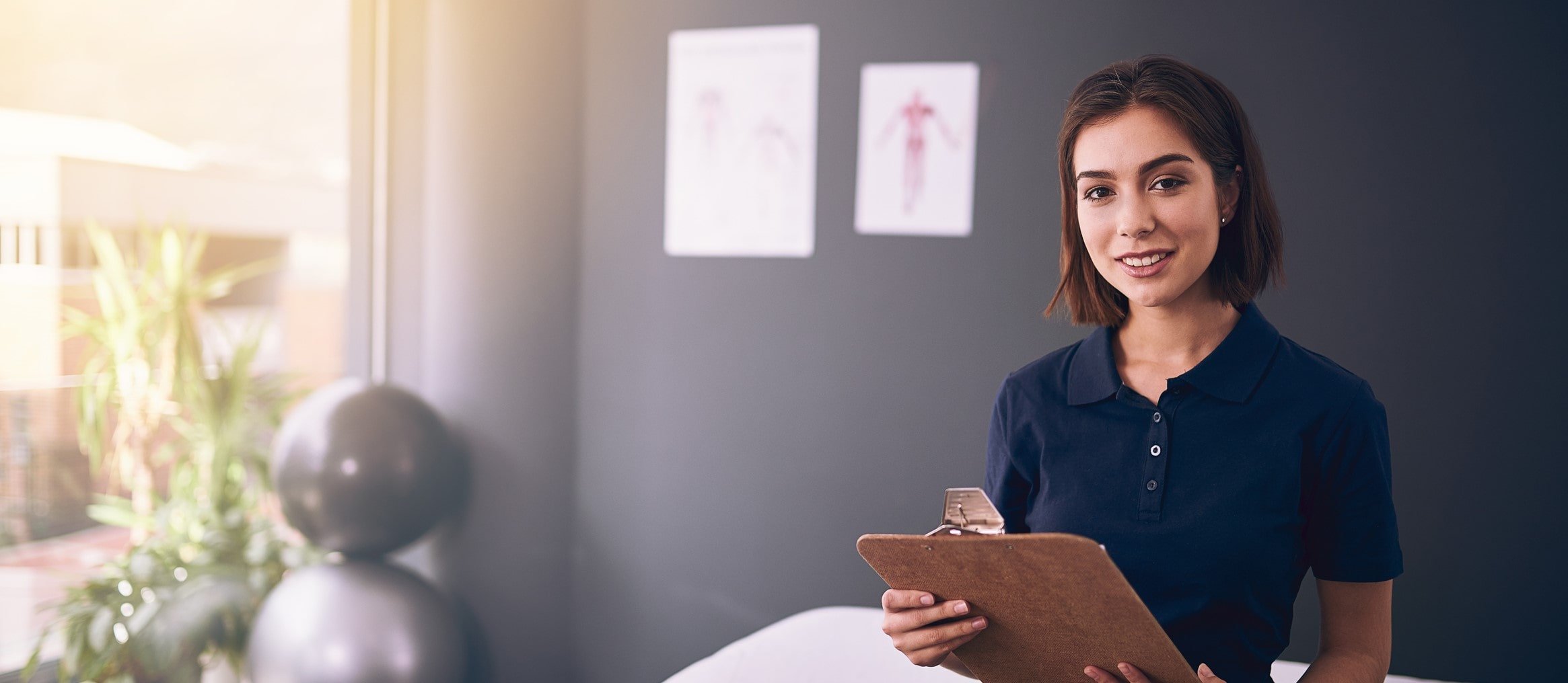 pretty young brunette physical therapist in blue shirt, holding clip board inside clinic exam room pretty young brunette physical therapist in blue shirt, holding clip board inside clinic exam room
