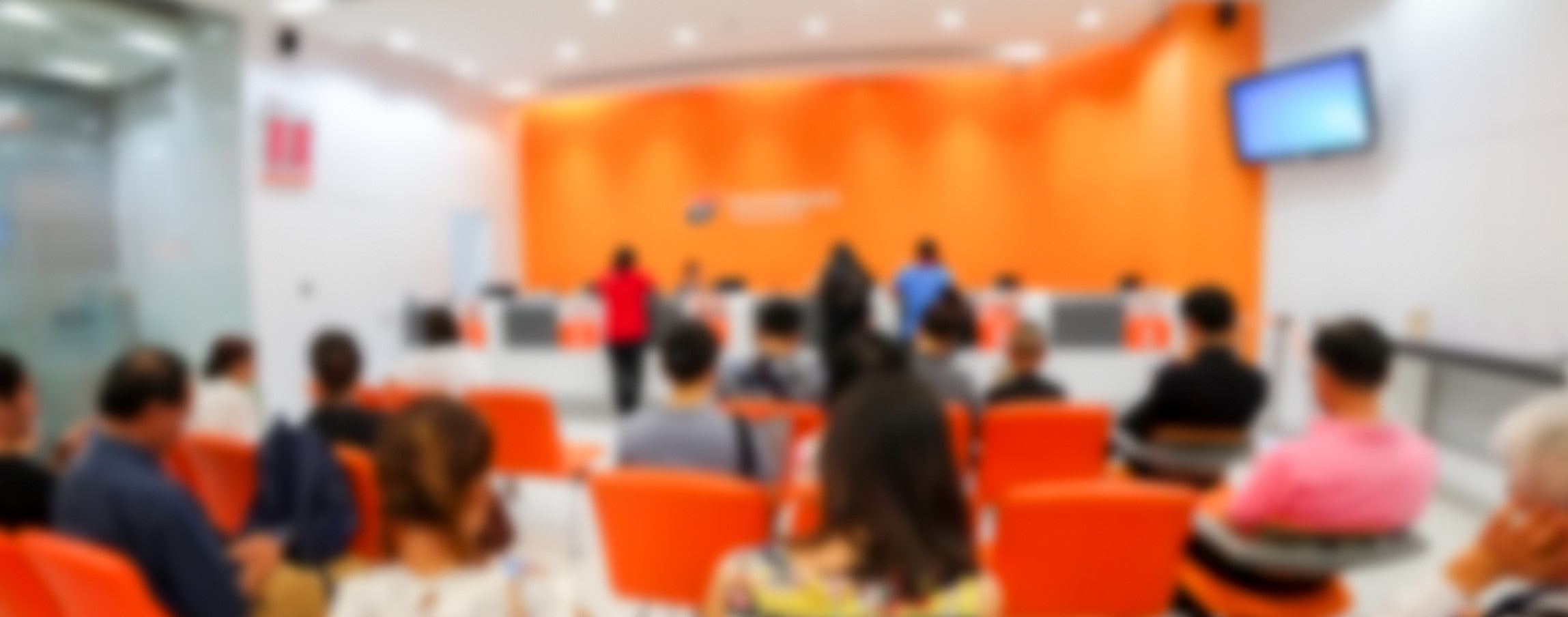 blurred shot of overcrowded emergency room with TVs on wall and orange backdrop at front of room blurred shot of overcrowded emergency room with TVs on wall and orange backdrop at front of room