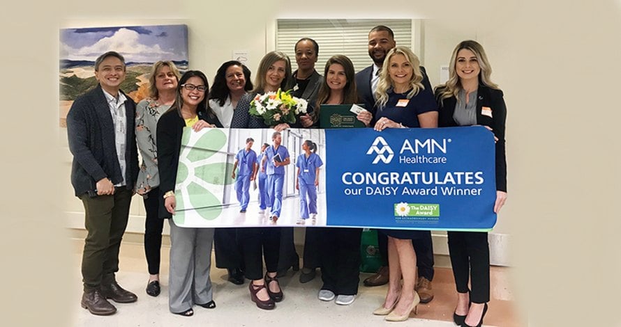 AMN Healthcare team holding a congratulations banner for the 2018 Daisy Nurse Award Winner