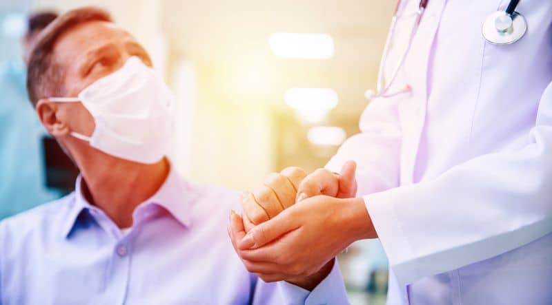 senior man with protective safety mask on face in a wheelchair and a confident doctor in the medical mask