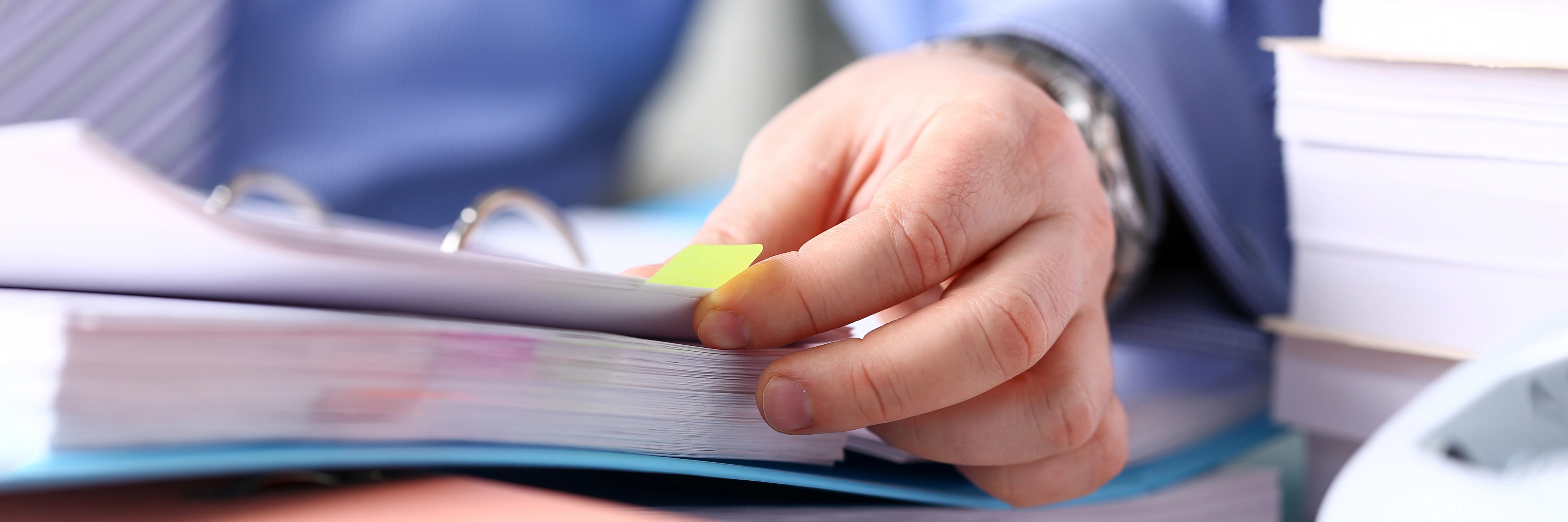 A person holding a yellow sticky note on a binder