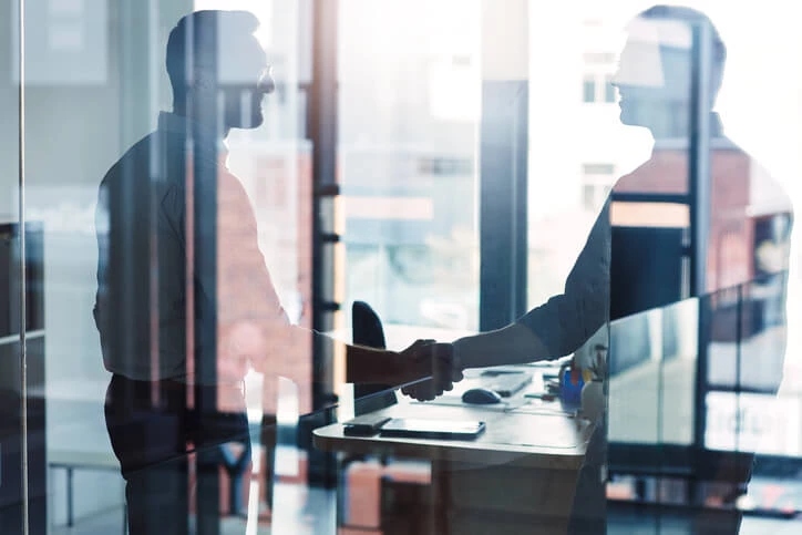 two men shaking hands in glass office