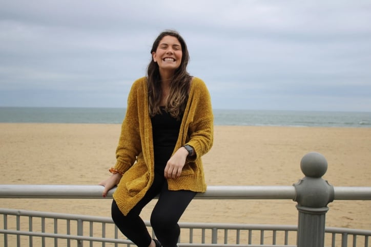 Woman smiling while sitting on a railing near a beach