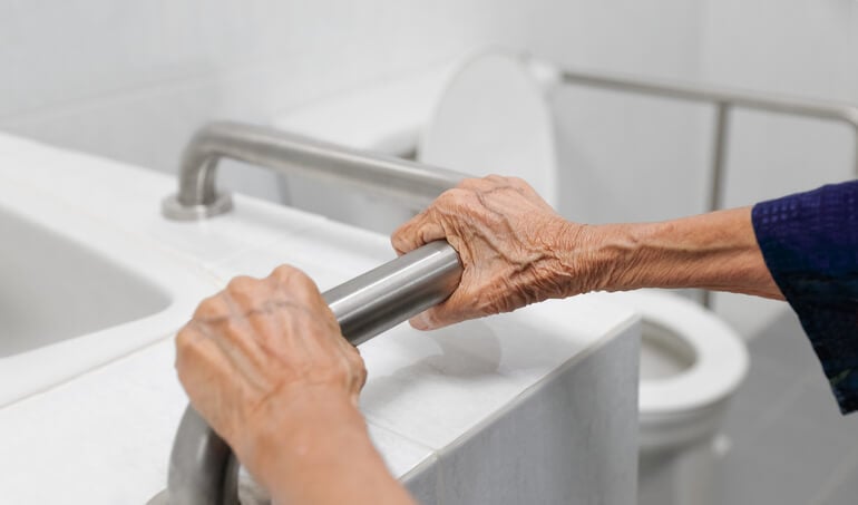 elderly woman gripping handrail in bathroom
