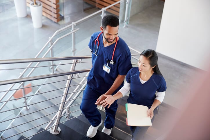 male and female healthcare professionals talking while climbing hospital stairs male and female healthcare professionals talking while climbing hospital stairs