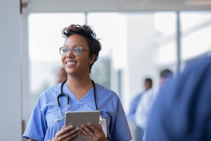 A nurse holding a tablet stands in a hallway A nurse holding a tablet stands in a hallway