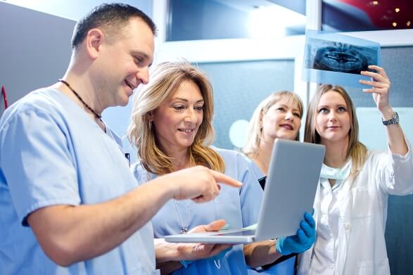 nurses looking at a laptop and a doctor examining an x-ray