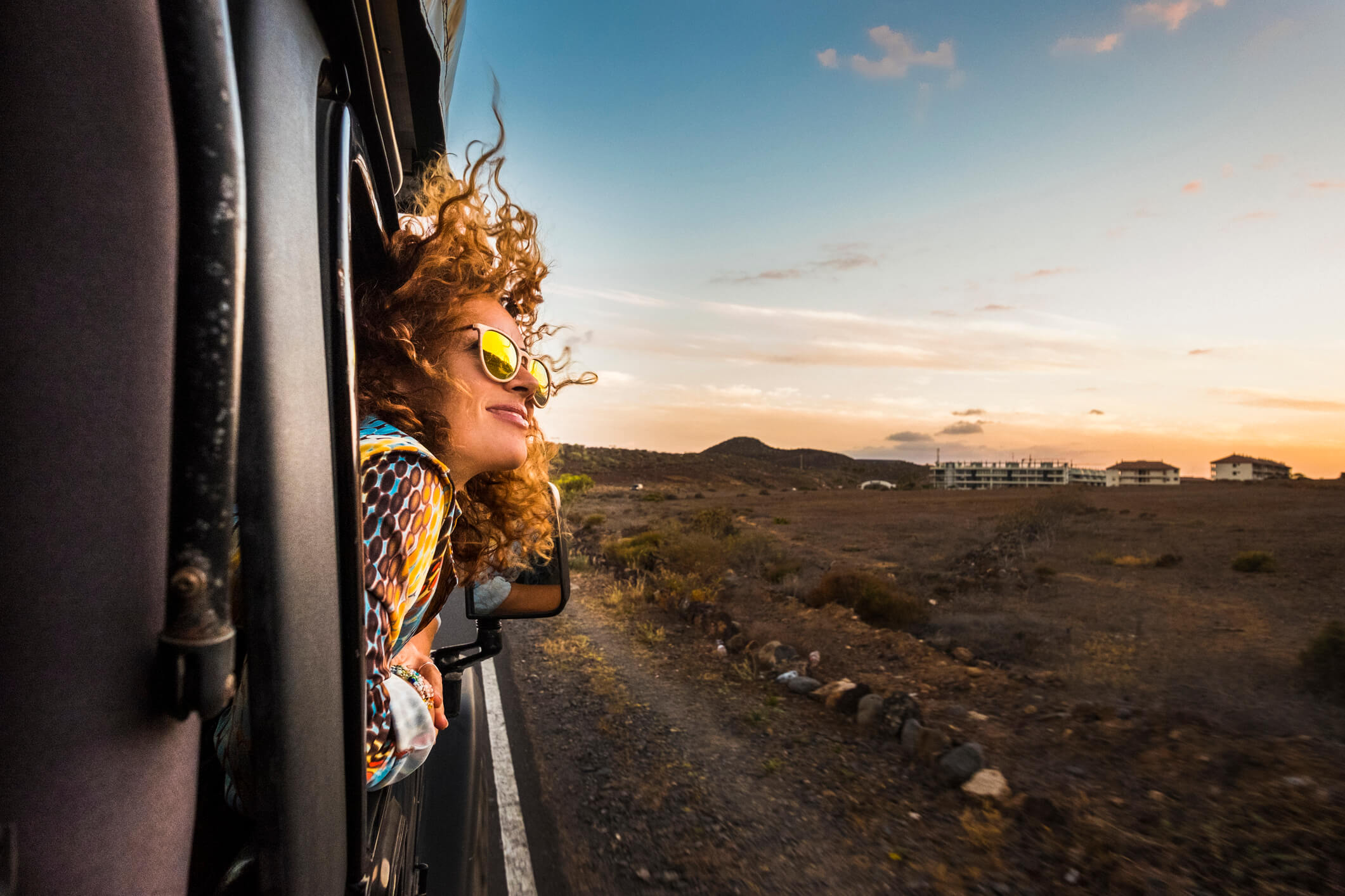 Woman peeking her head out from a moving car looking at beautiful scenery