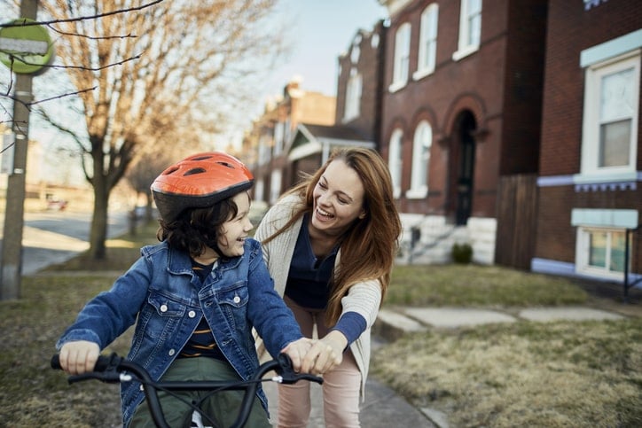 Happy mom guiding child as he rides his bike